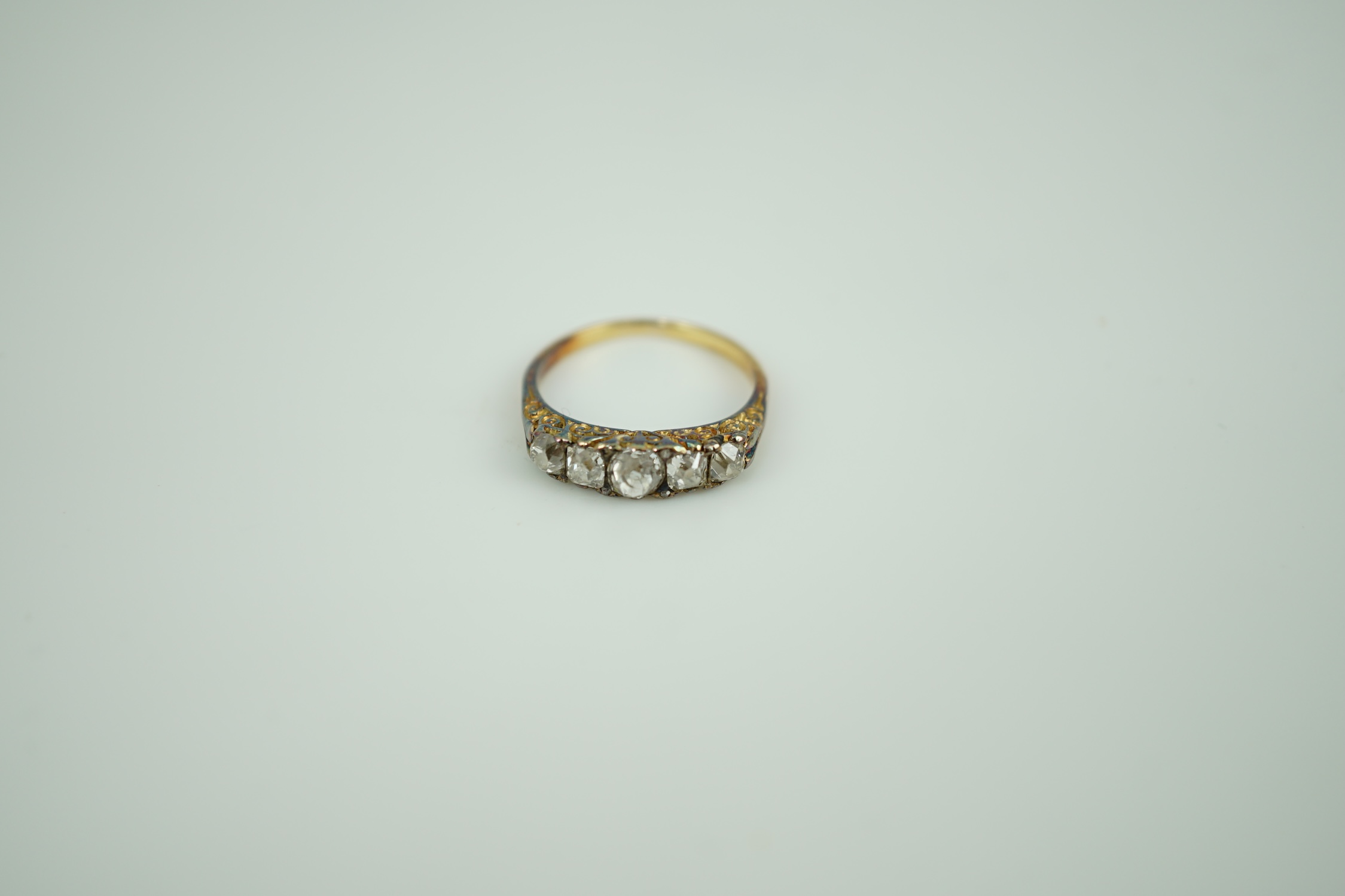 An early 20th century yellow metal and graduated five stone old round cut diamond set half hoop ring, with diamond chip spacers, size K, gross weight 2.8 grams.